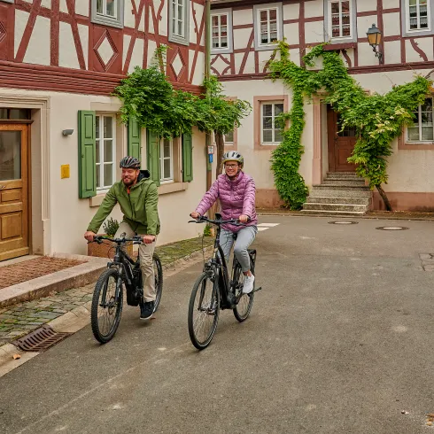 Zwei Personen fahren mit dem Rad entlang Fachwerkhäuser im Appelbachtal.