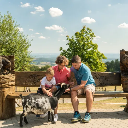 Eine Familie sitzt beim Wildpark Potzberg auf einer Bank und streicheln eine Ziege.