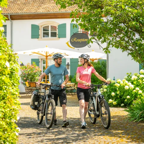 Zwei Personen schieben ihre Fahrräder aus einer Unterkunft in der Pfalz und starten zu eine Radtour.