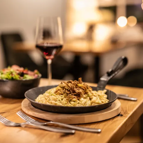 Auf einem Restauranttisch stehen Spätzle in einer Gusspfanne, ein Beilagensalat und ein Glas Rotwein.