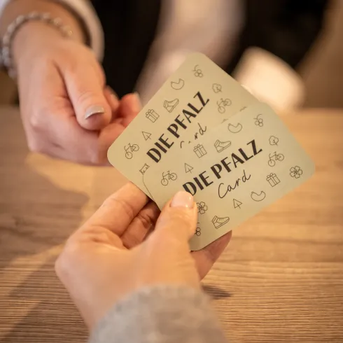 Eine Person reicht einer anderen Person zwei Karten auf denen "Die Pfalzcard" steht.