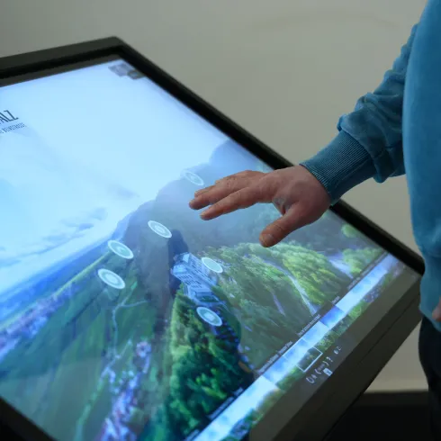 ine Person bedient eine digitale Stele, auf deren Bildschirm eine Luftaufnahme der Pfalz ist.