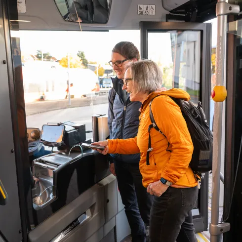 Zwei Personen zeigen ihre Tickets einem Busfahrer vor.