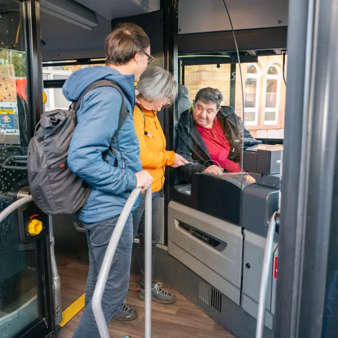 Zwei Personen zeigen ihr Ticket einem Busfahrer vor.