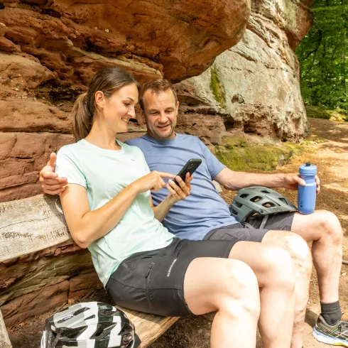 Zwei Personen sitzen auf einer Bank vor einem Felsen.