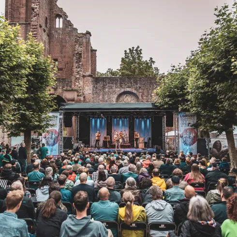 Besuchende des Limburg Sommer in Bad Dürkheim sitzen vor einer Bühne, auf der eine Band spielt.